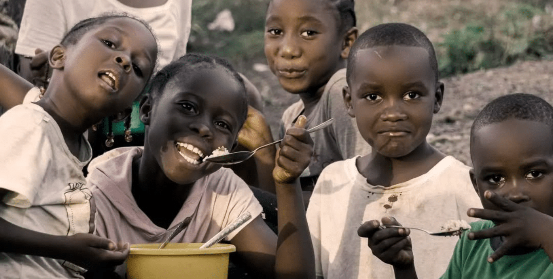Six African children looking directly forward, a couple eating rice with spoons