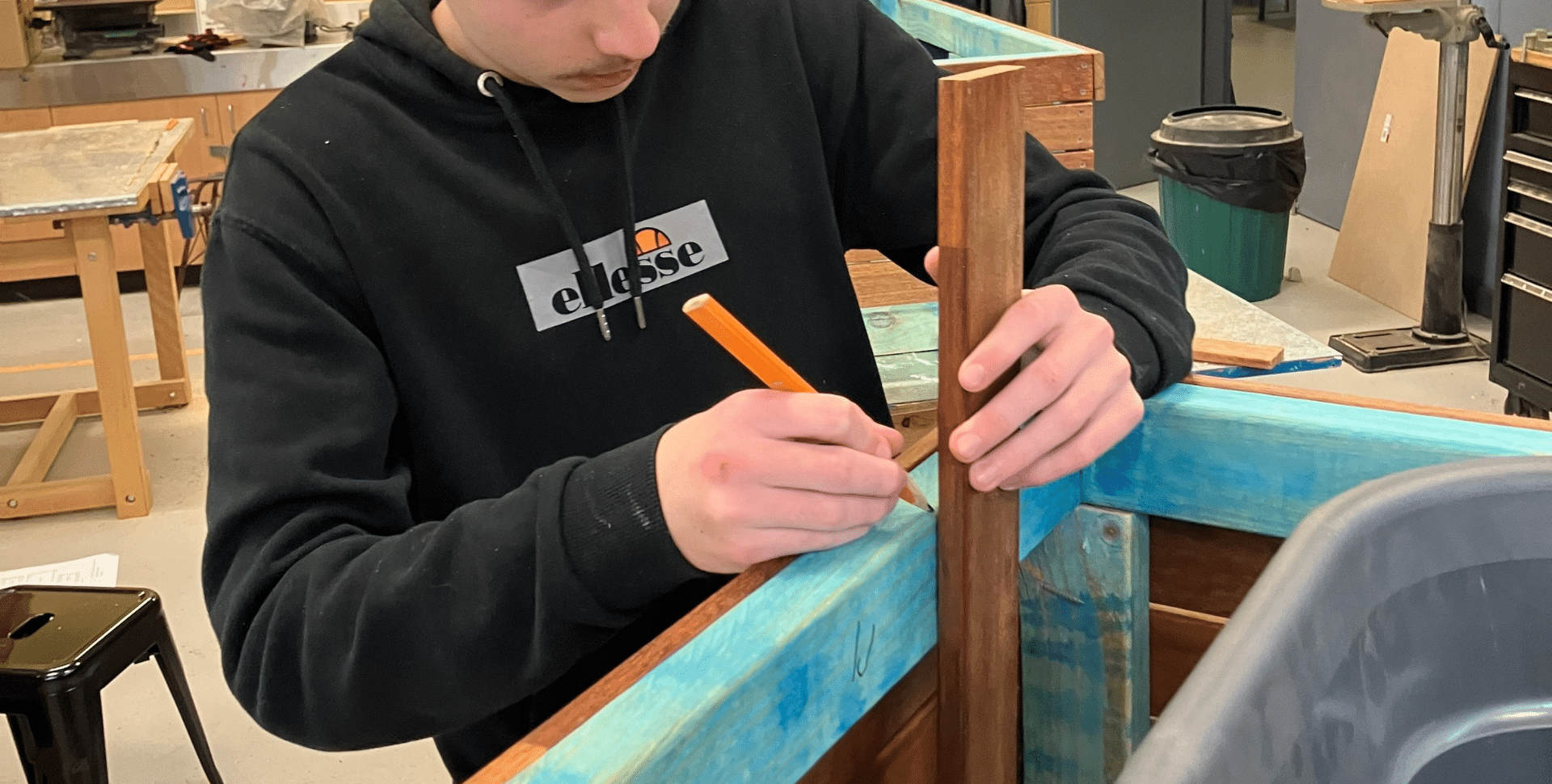 young person marks a measurement on the side of a woodworking project