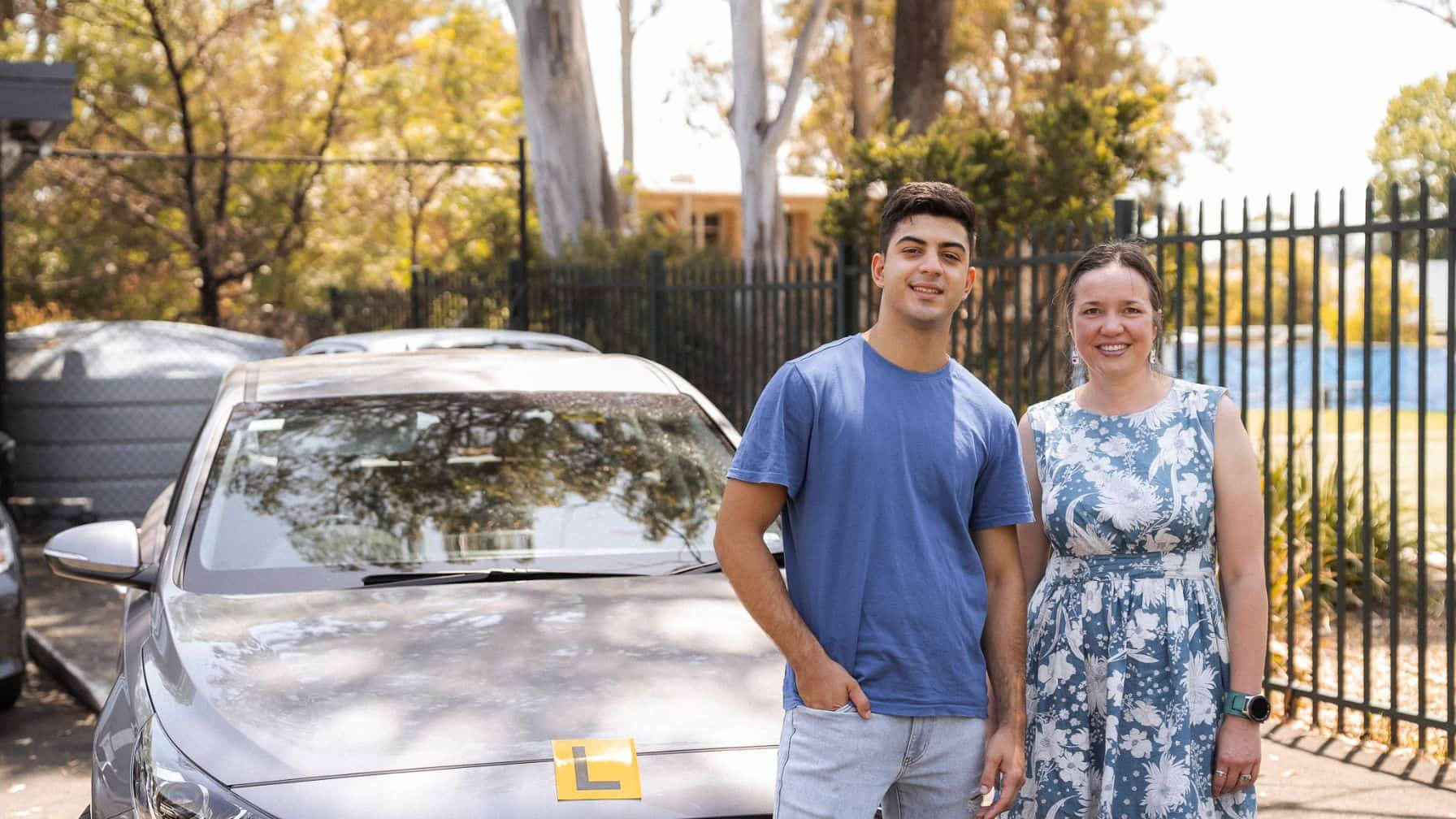 Teenage boy standing with female driving instructor in front of car