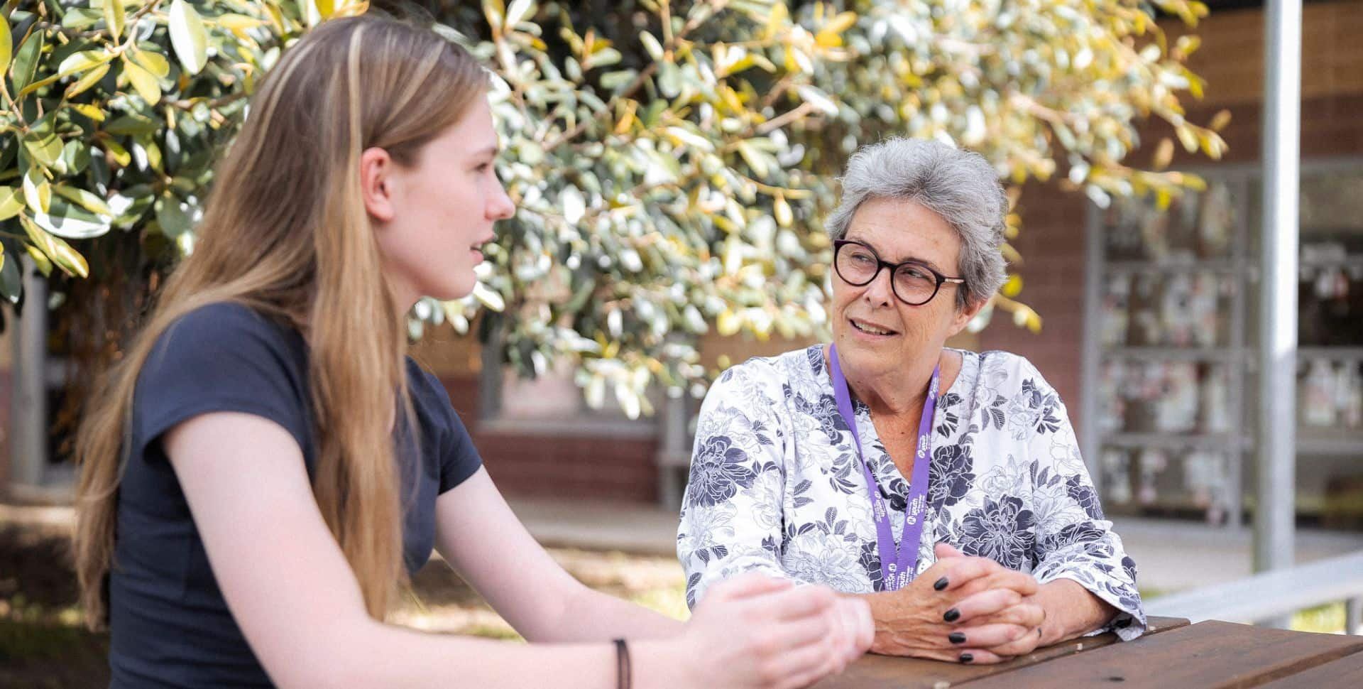 Older woman with glasses counselling teenage girl at picnic table