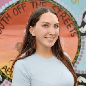 First Nations Australian girl standing in front of Indigenous artwork